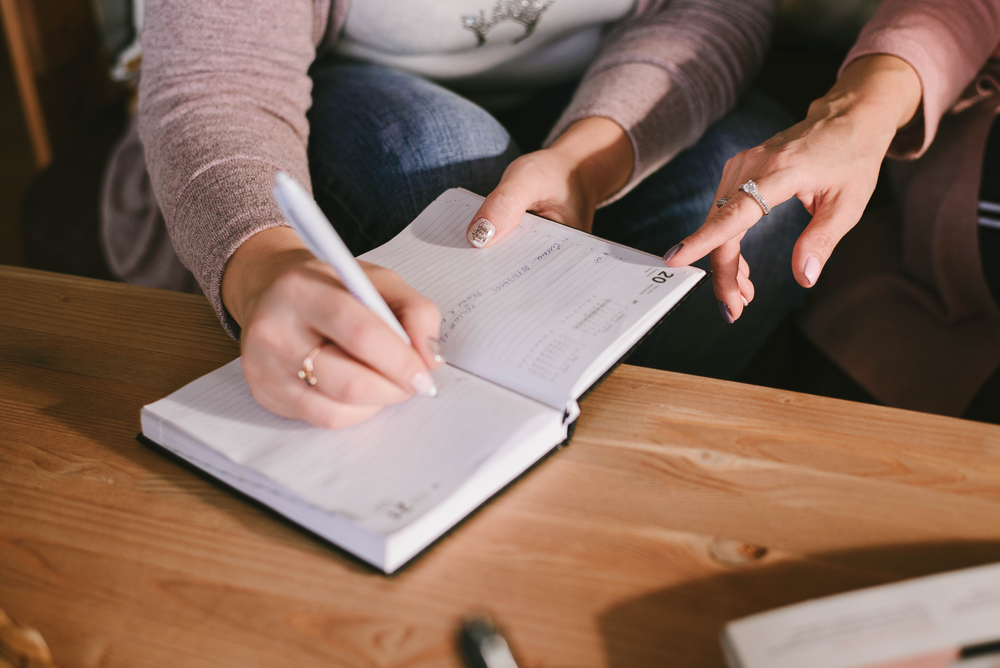 hands and diary. Two women are discussing and writing something down. Business